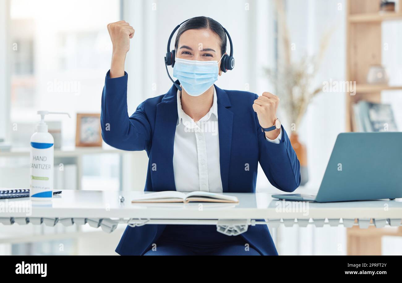 Customer service, call center and telemarketing agent celebration while wearing mask and headset working on a laptop alone at work. Business woman cheering for sale success at a desk in an office Stock Photo