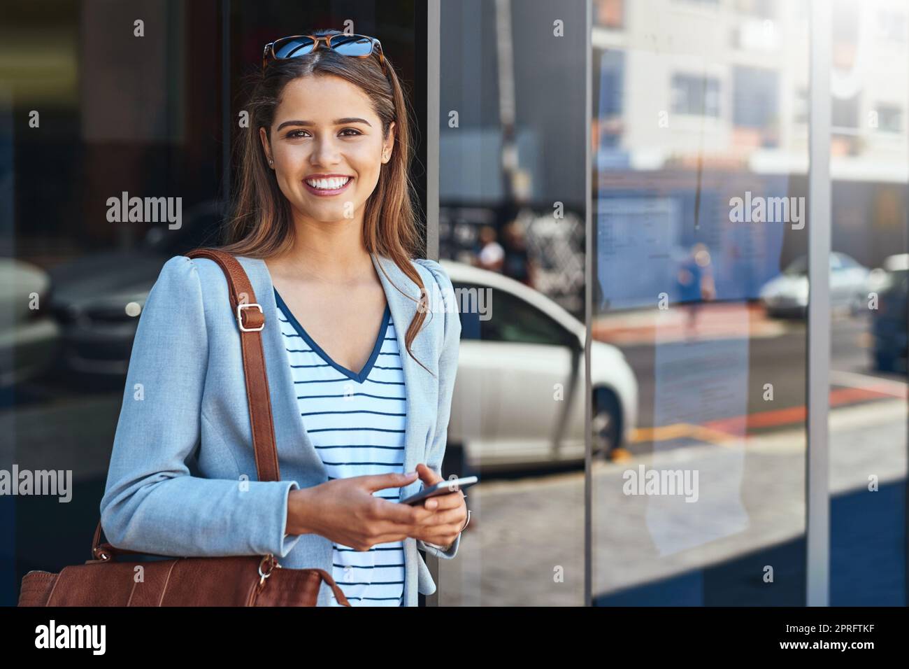 Thats work done for the day. Cropped portrait of an attractive young woman using her cellphone while leaving the office. Stock Photo
