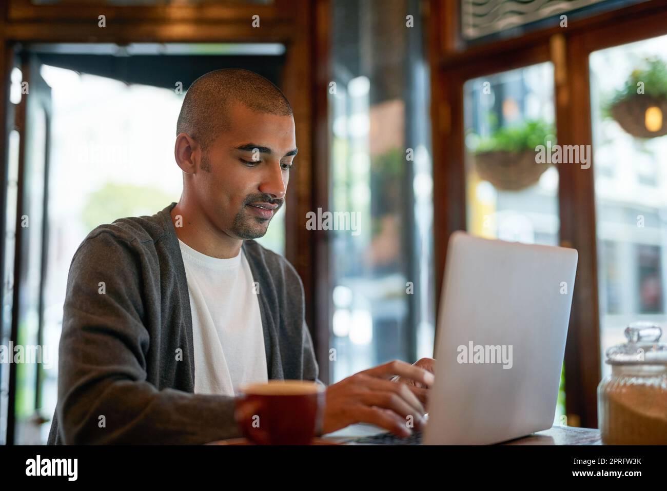 This is his perfect working environment to stay productive. a young man working on his laptop in a cafe. Stock Photo