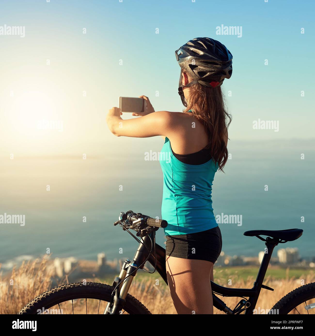 Mountain biking is an escape. a young woman taking a picture of the beautiful scenery while out mountain biking. Stock Photo