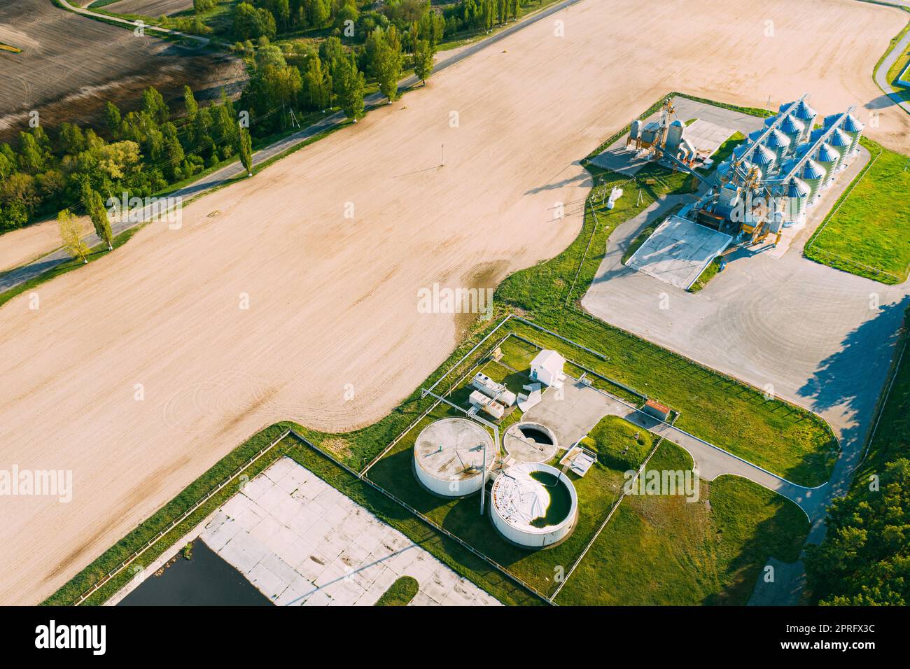 Biogas Bio-gas Plant From Pig Farm And Granary, Grain-drying Complex, Commercial Grain Or Seed Silos In Sunny Spring Rural Landscape. Corn Dryer Silos, Inland Grain Terminal, Elevators Stock Photo
