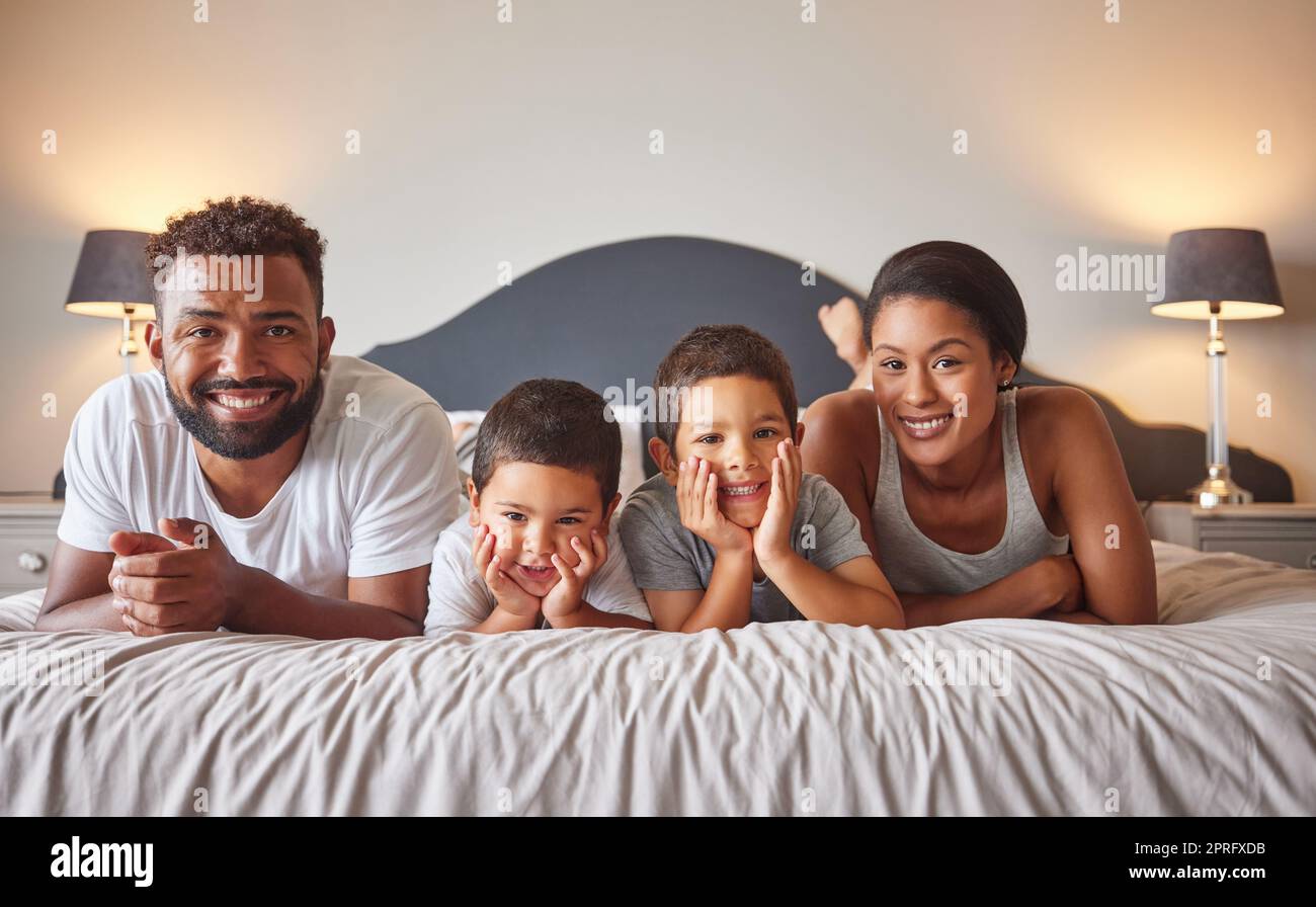 Portrait of parents and kids lying on bed in the morning with a smile. Playful, fun, mom and dad playing indoors showing growth, child development, happiness and childhood innocence from little boys Stock Photo