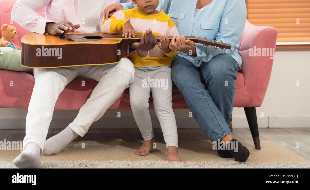 Happy family playing guitar together on the couch in living room at home. Stock Photo