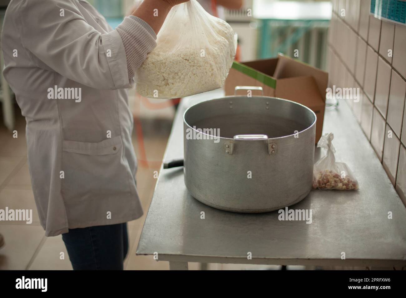 Cook prepares meals. Large pot on table. Cottage cheese in bag. Work as