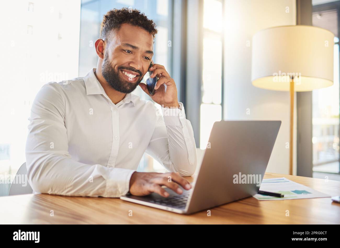 Management, planning and networking phone call by happy business man. Talking to client while working on a laptop in corporate office. Professional worker checking an online calendar for appointment Stock Photo