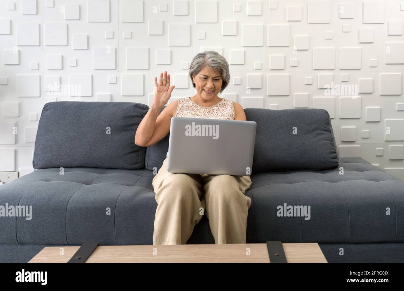Asian gray hair old woman waving hand via remote communication through laptop computer in the living room. Stock Photo