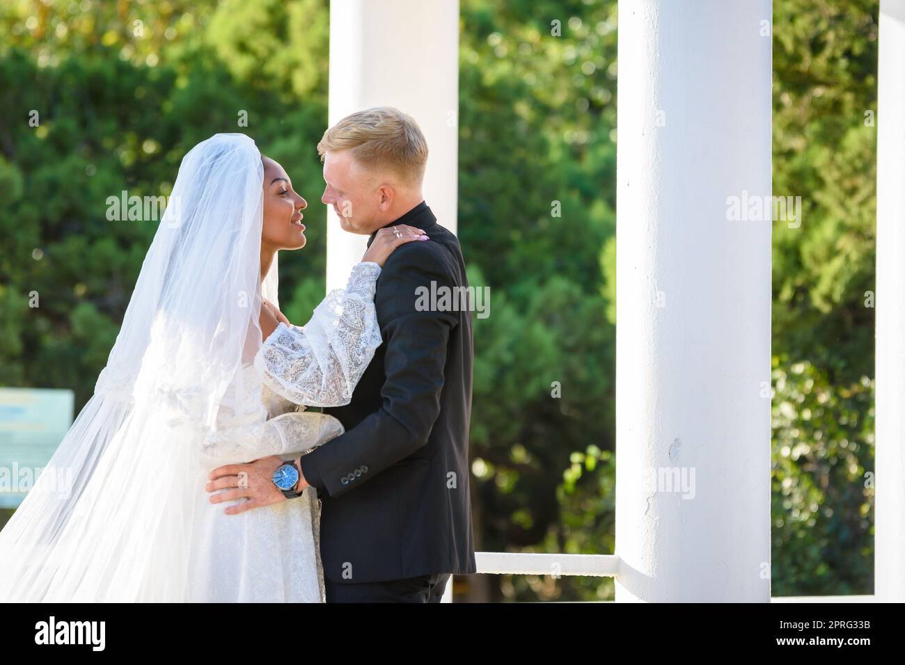Mixed-racial newlyweds on a walk hugging and lovingly look at each other Stock Photo