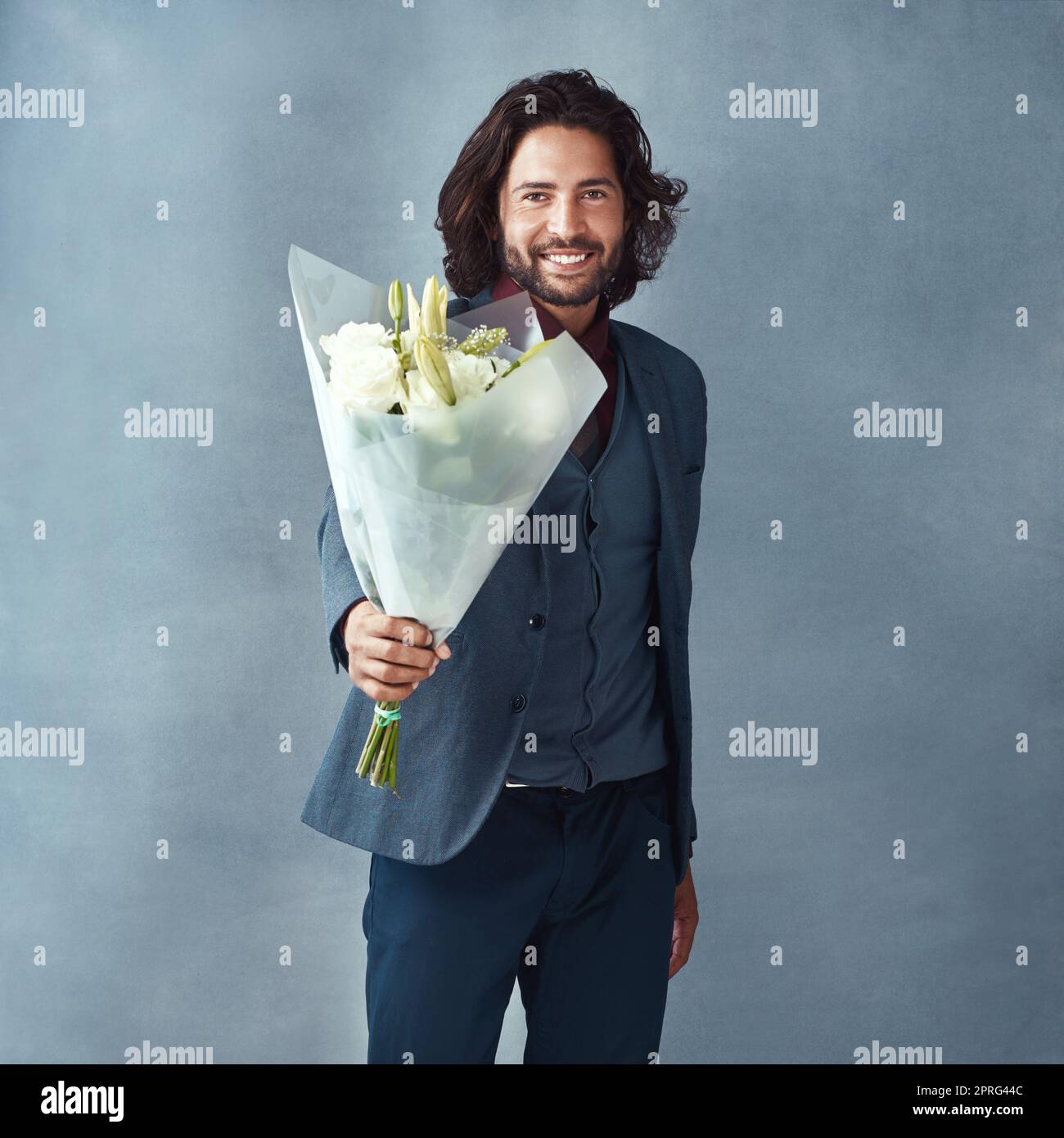 He knows how to turn up the romance. Studio shot of a stylishly dressed handsome young man holding a bouquet of flowers against a gray background. Stock Photo