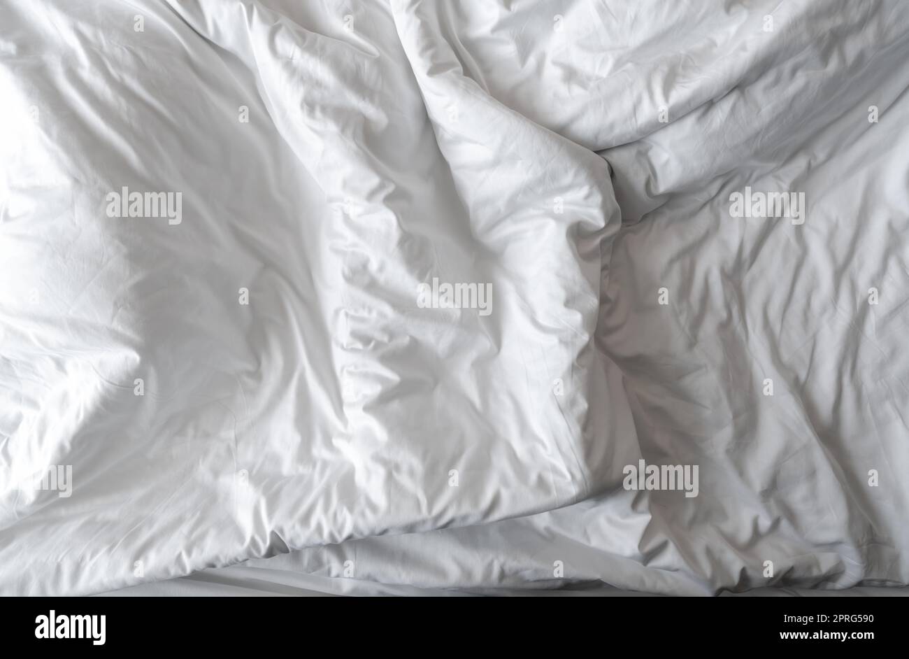 White linen blanket in hotel bedroom. Close-up detail of messy white blanket. Comfortable bed with soft white duvet. Sleep tight with good quality bedding household concept. Wrinkled white blanket. Stock Photo