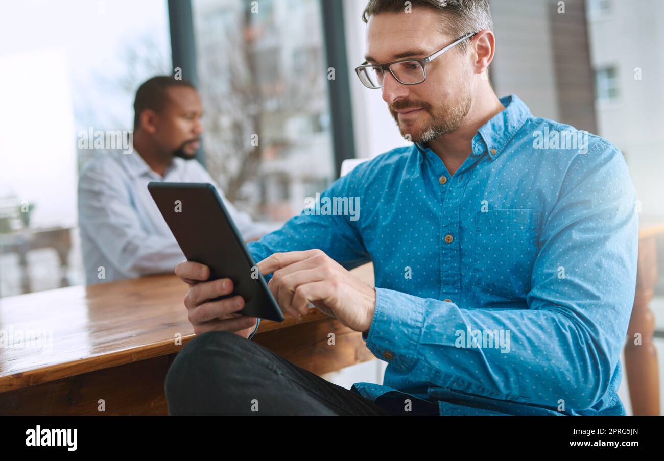 Getting to grips with his new work tool. a businessman using his tablet with a colleague in the background. Stock Photo