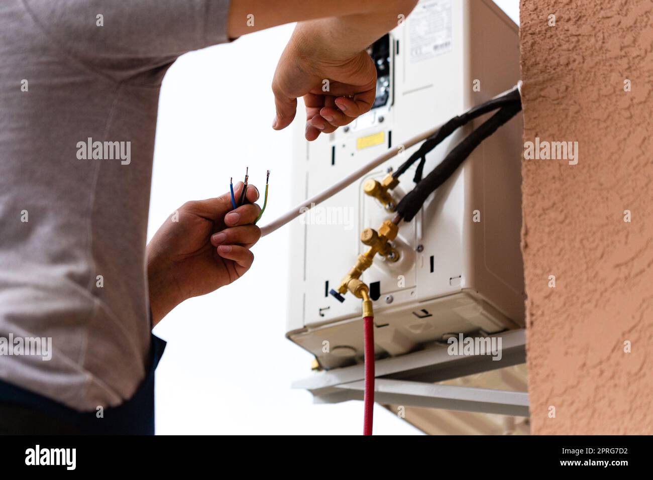 Male worker connects electrical wires during installation of air conditioner. Stock Photo