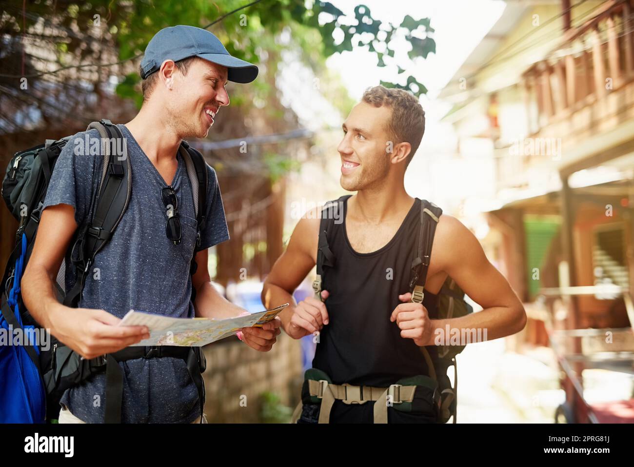 Theyve got places to see. two smiling young friends wearing backpacks traveling talking together over a map while in Thailand. Stock Photo