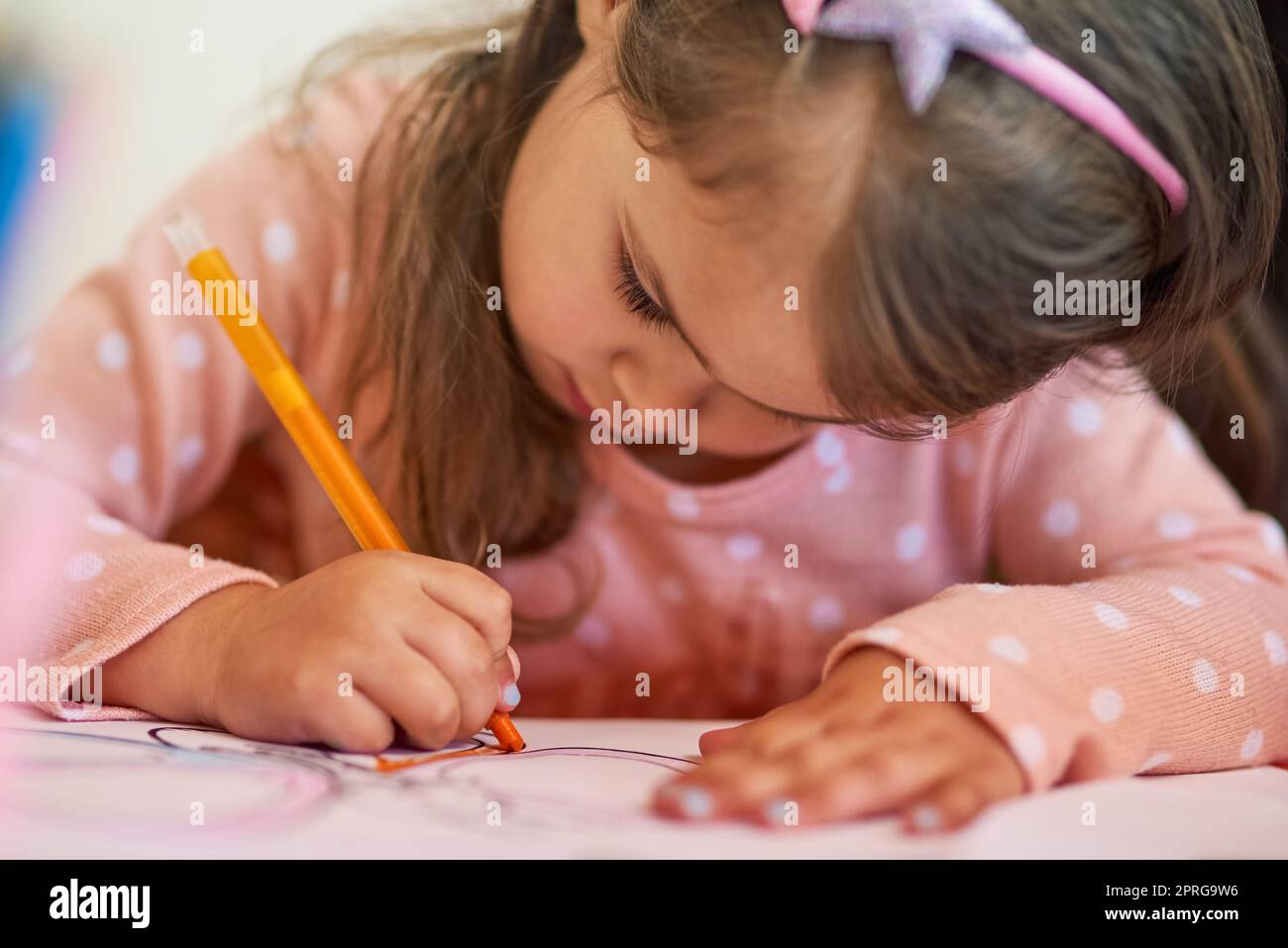 Colouring in is her favourite hobby. a little girl colouring in a picture at home. Stock Photo