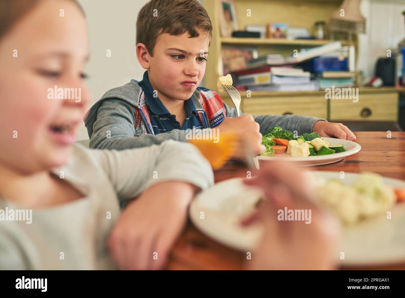 What is this stuff, anyway. two grumpy children refusing to eat their vegetables. Stock Photo