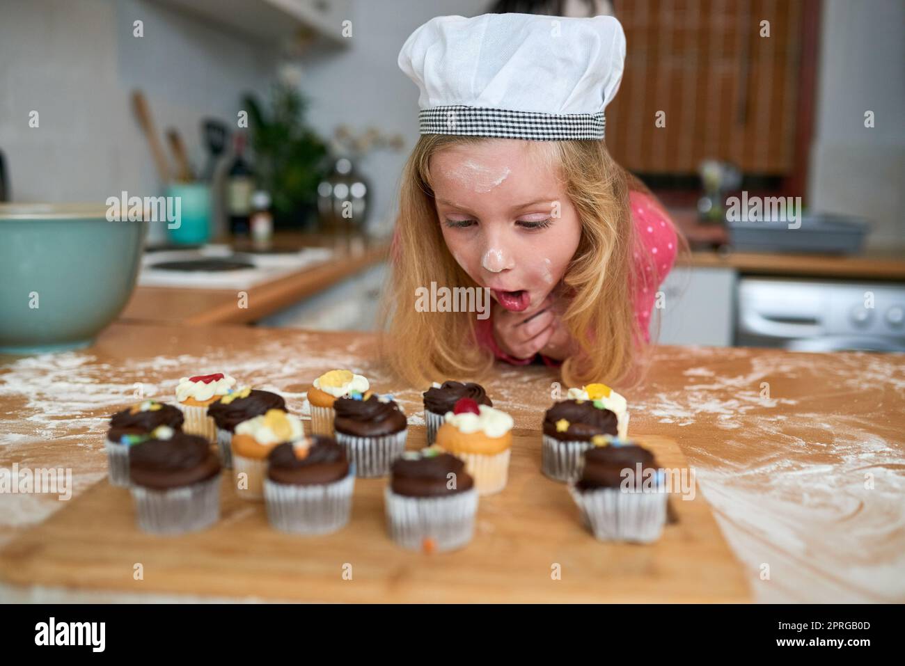 They look so delicious. a surprised little girl looking at cupcakes she baked at home. Stock Photo