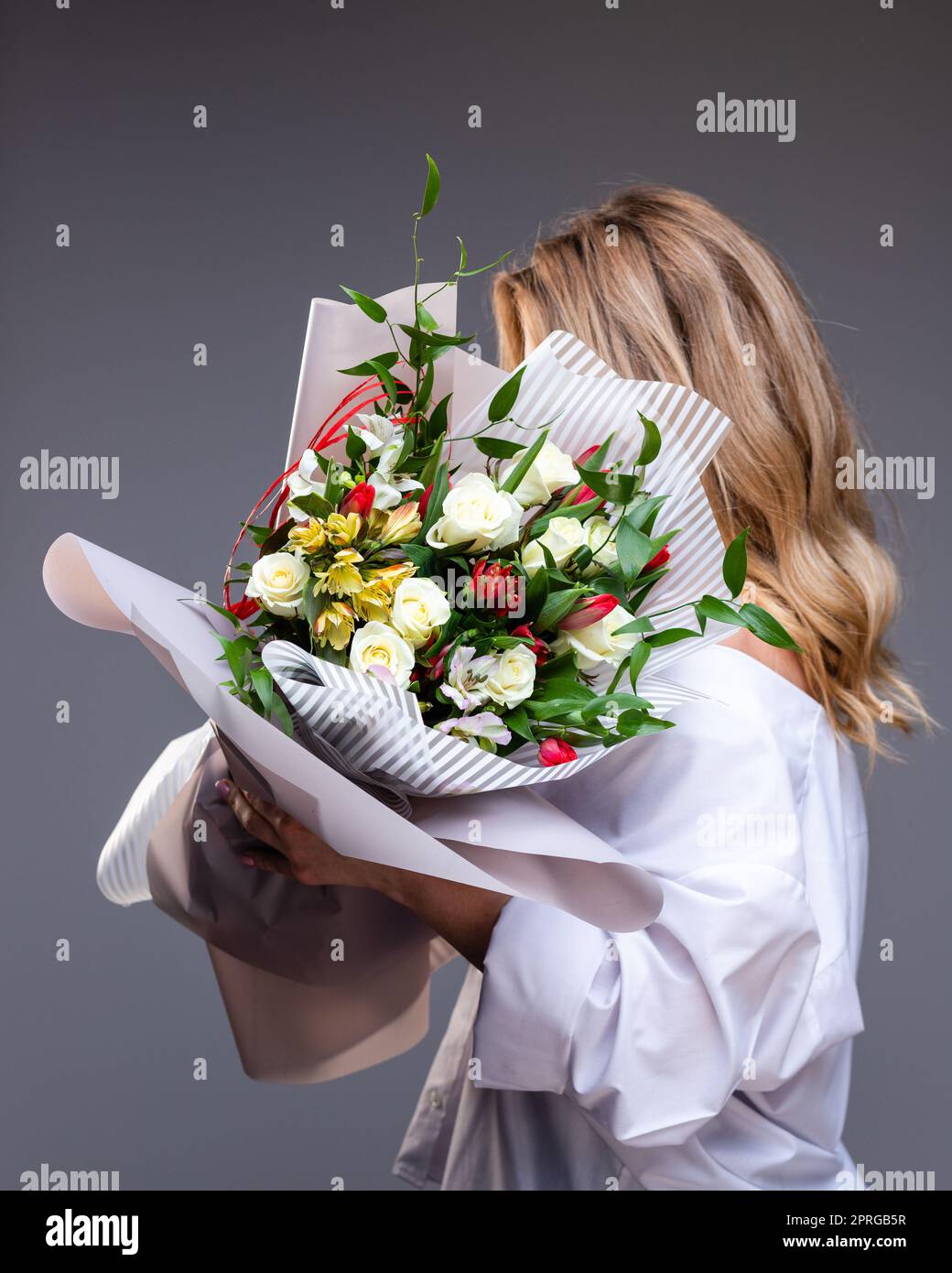 Woman in a white shirt holds a bouquet of flowers with roses, tulips and greenery. Stock Photo