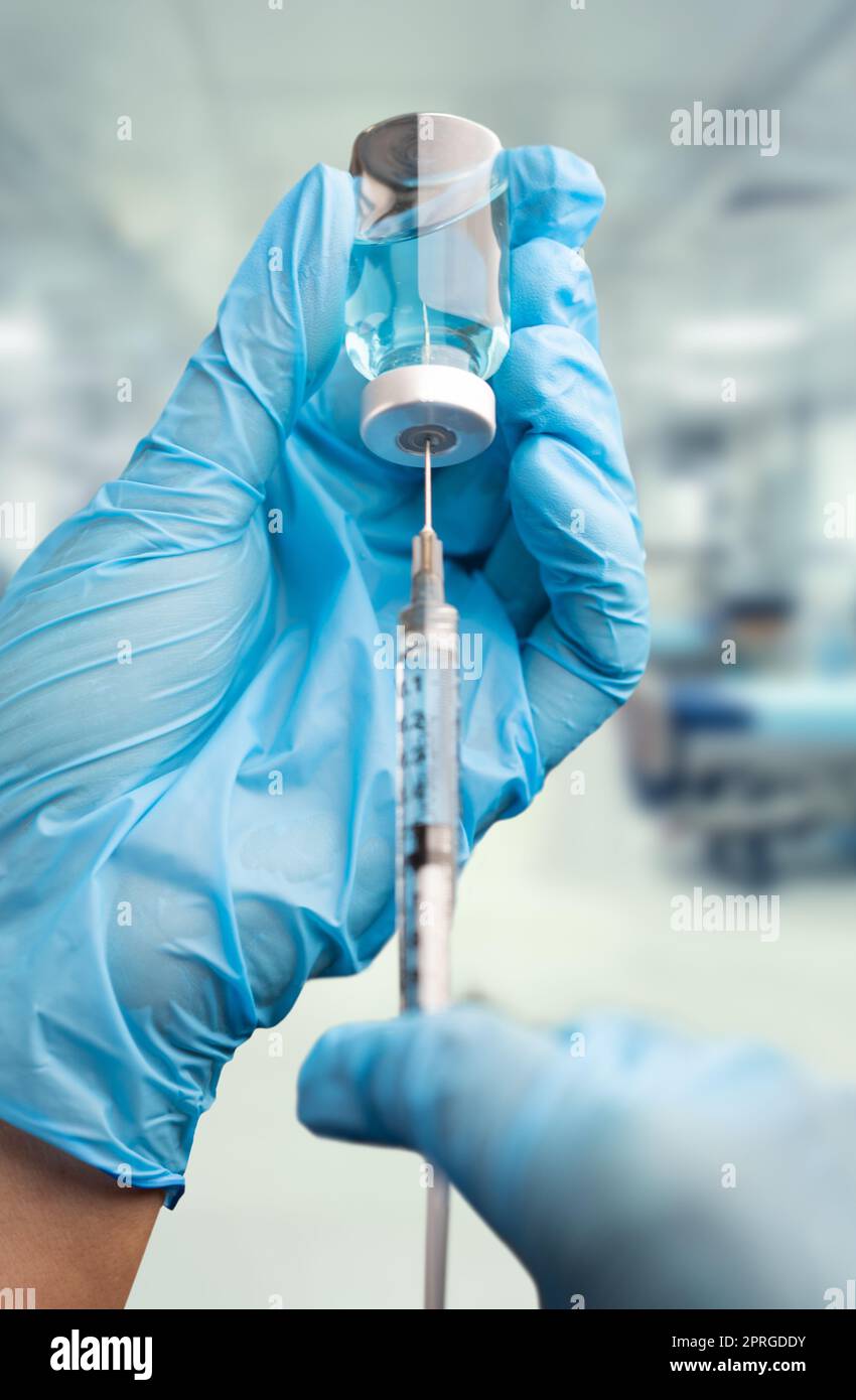 Doctor or Nurse Wearing Surgical Gloves Holding Vaccine Vial and Medical Syringe Within Hospital. Stock Photo