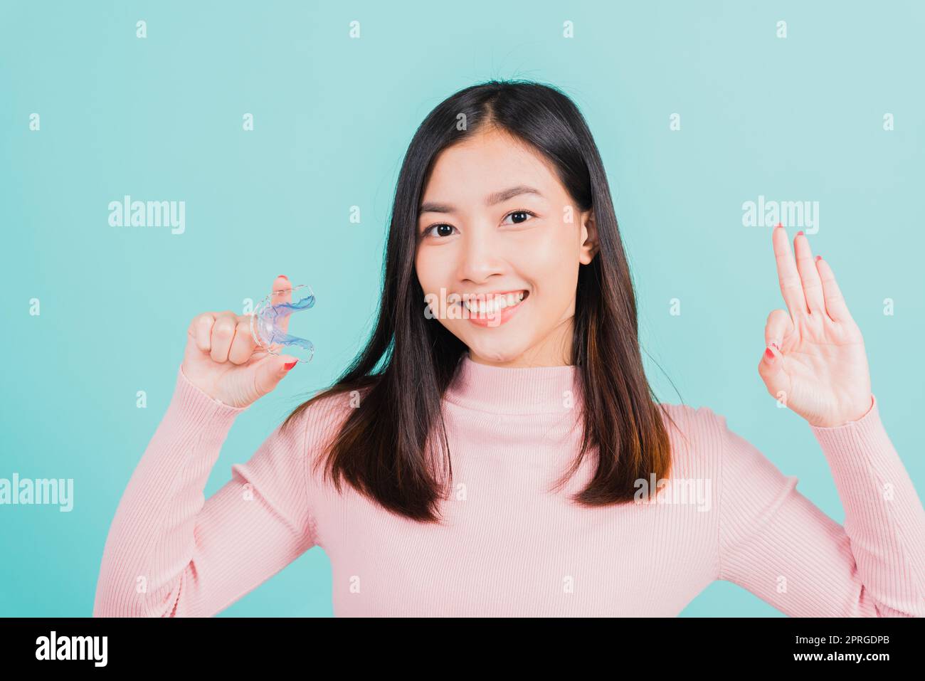 woman smiling holding silicone orthodontic retainers for teeth and show finger brackets saying OK sign Stock Photo