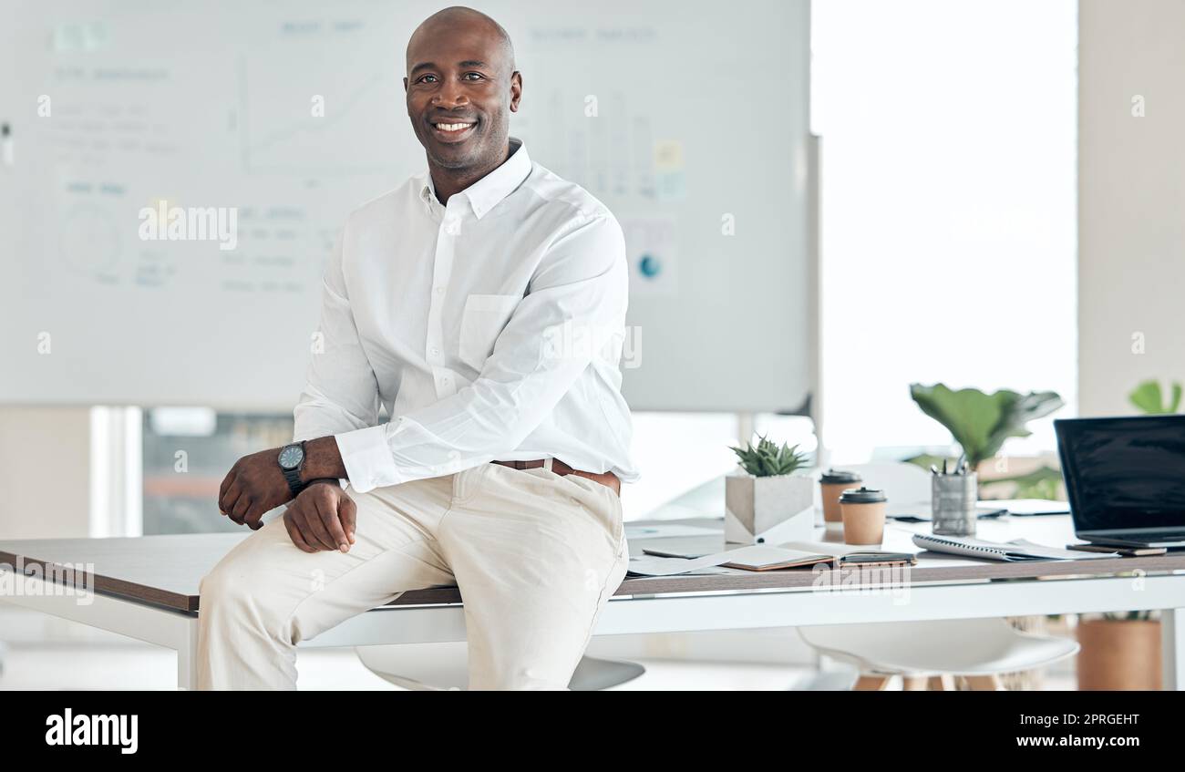 Black business man, leader and office in happy, proud and confident success for company goals in the corporate workplace. African guy in success at desk with smile in management and leadership work Stock Photo