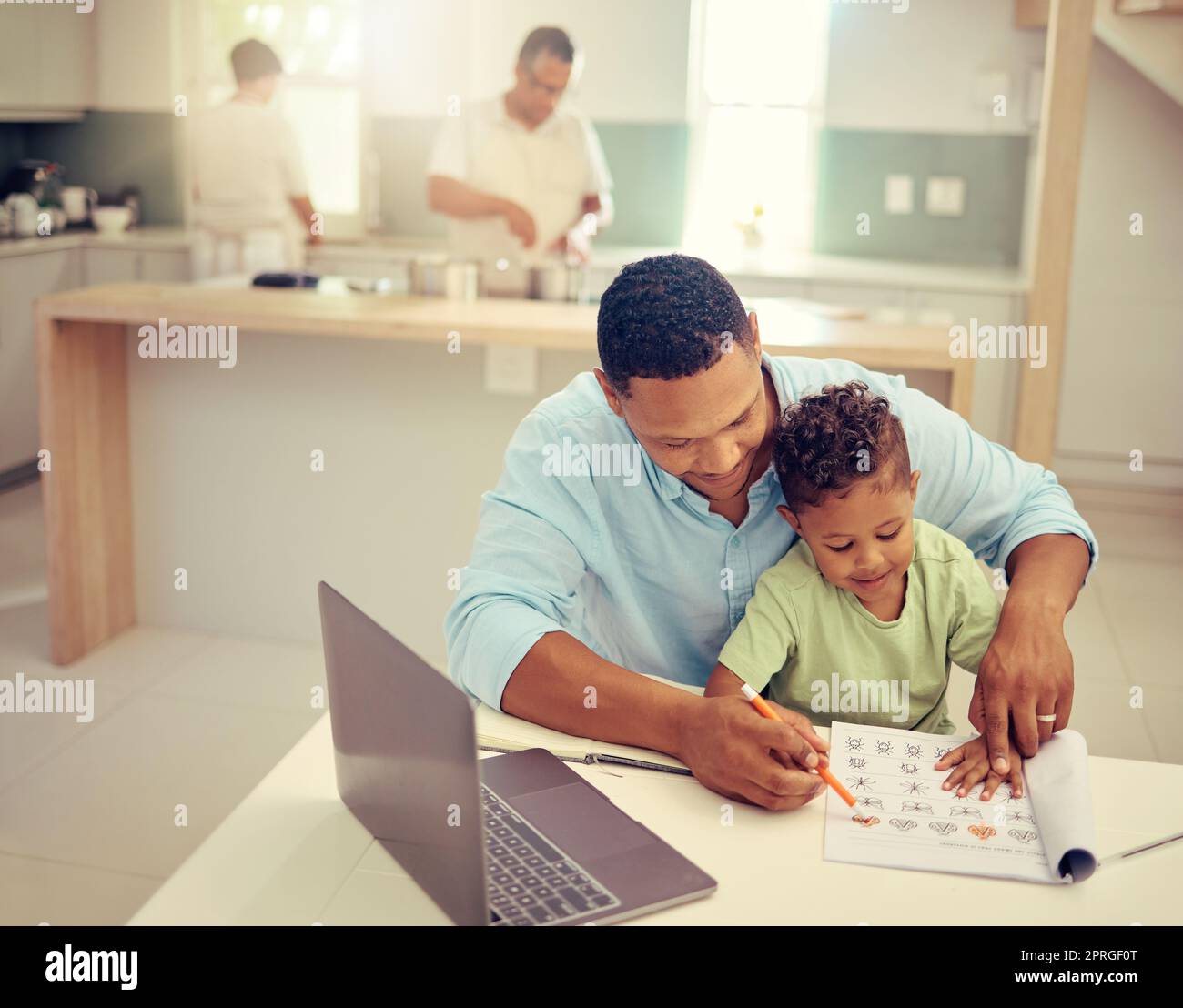 Father, child and learning to color in a book, helpful dad teaching son to hold a pencil at home. Happy family man helping his kid with homework on break from working on laptop in the kitchen. Stock Photo