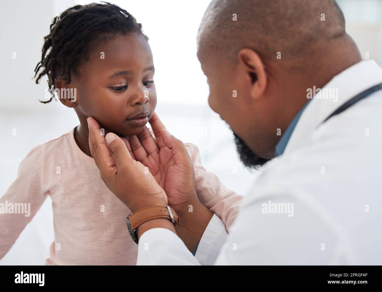Medical doctor checking a girl throat with care in his office at a modern surgery center. Man pediatrician touching the patients neck during healthcare, medicare and illness consultation at clinic Stock Photo
