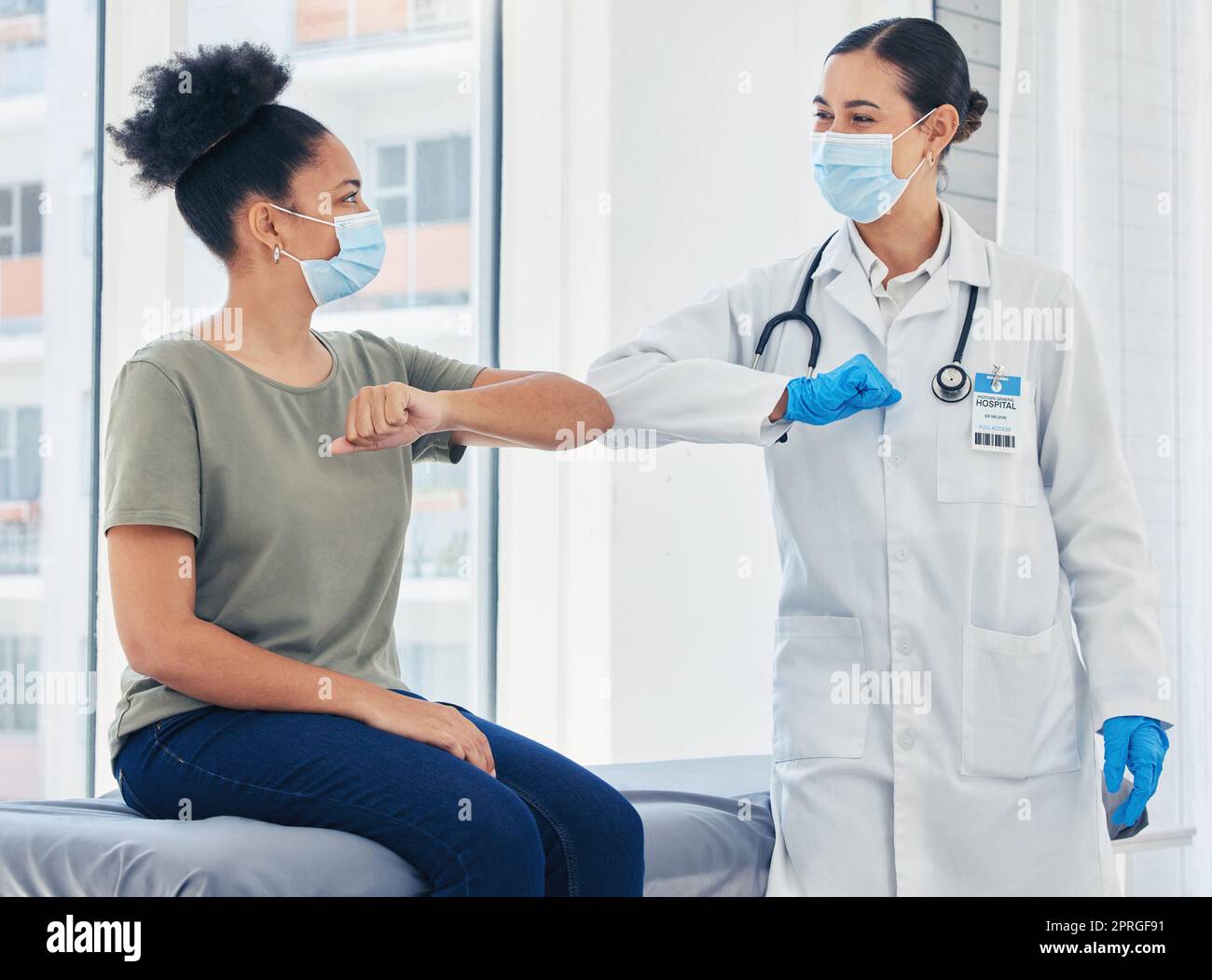 Doctor, covid and greeting medical healthcare expert with patient in safe elbow with masks in a hospital. Happy women following safety social distance rules to prevent the spread of virus at clinic Stock Photo