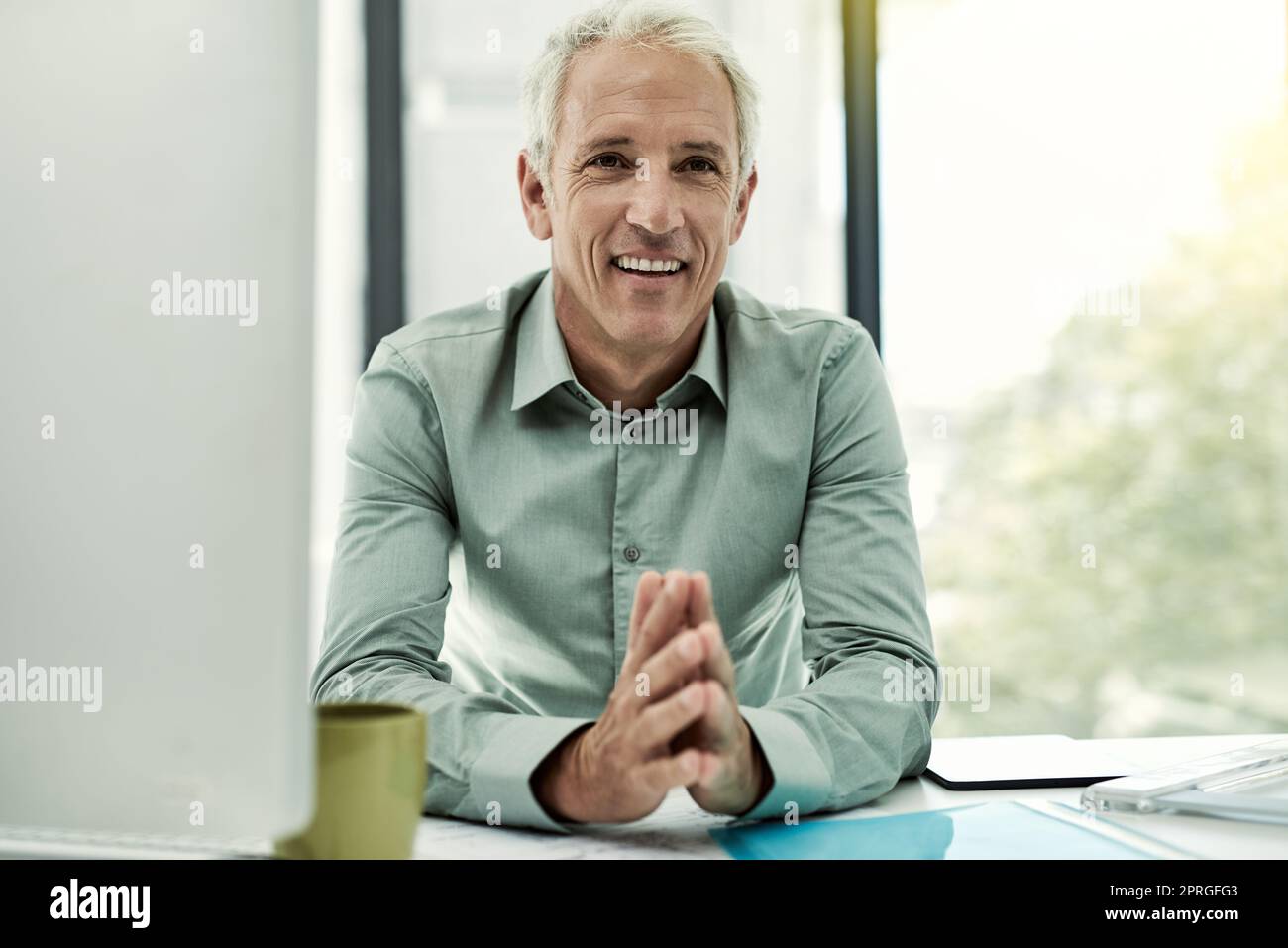 He has an easygoing approach to business. Portrait of a mature businessman working at his desk in an office. Stock Photo