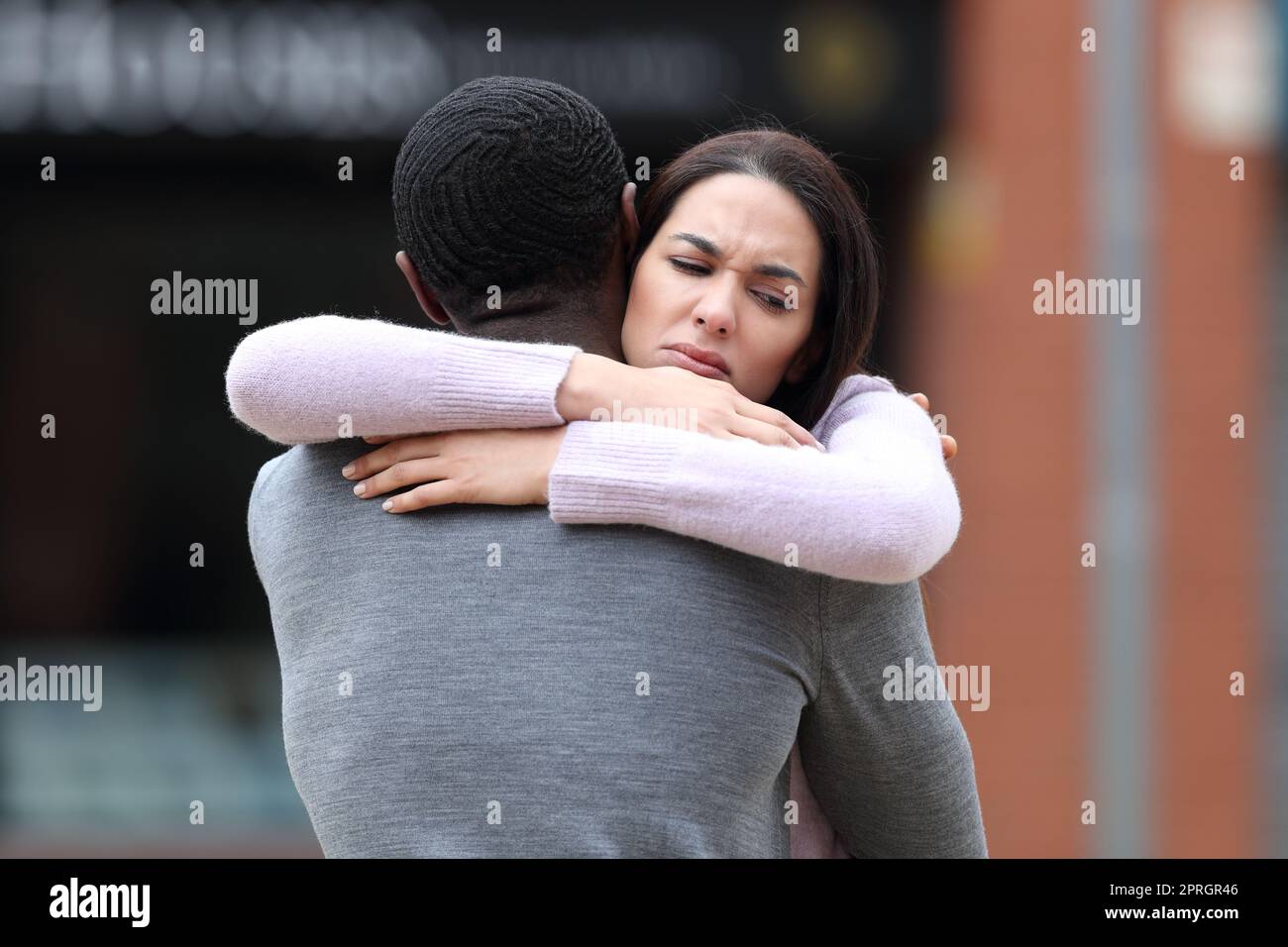 Disappointed woman hugging a black man in the street Stock Photo