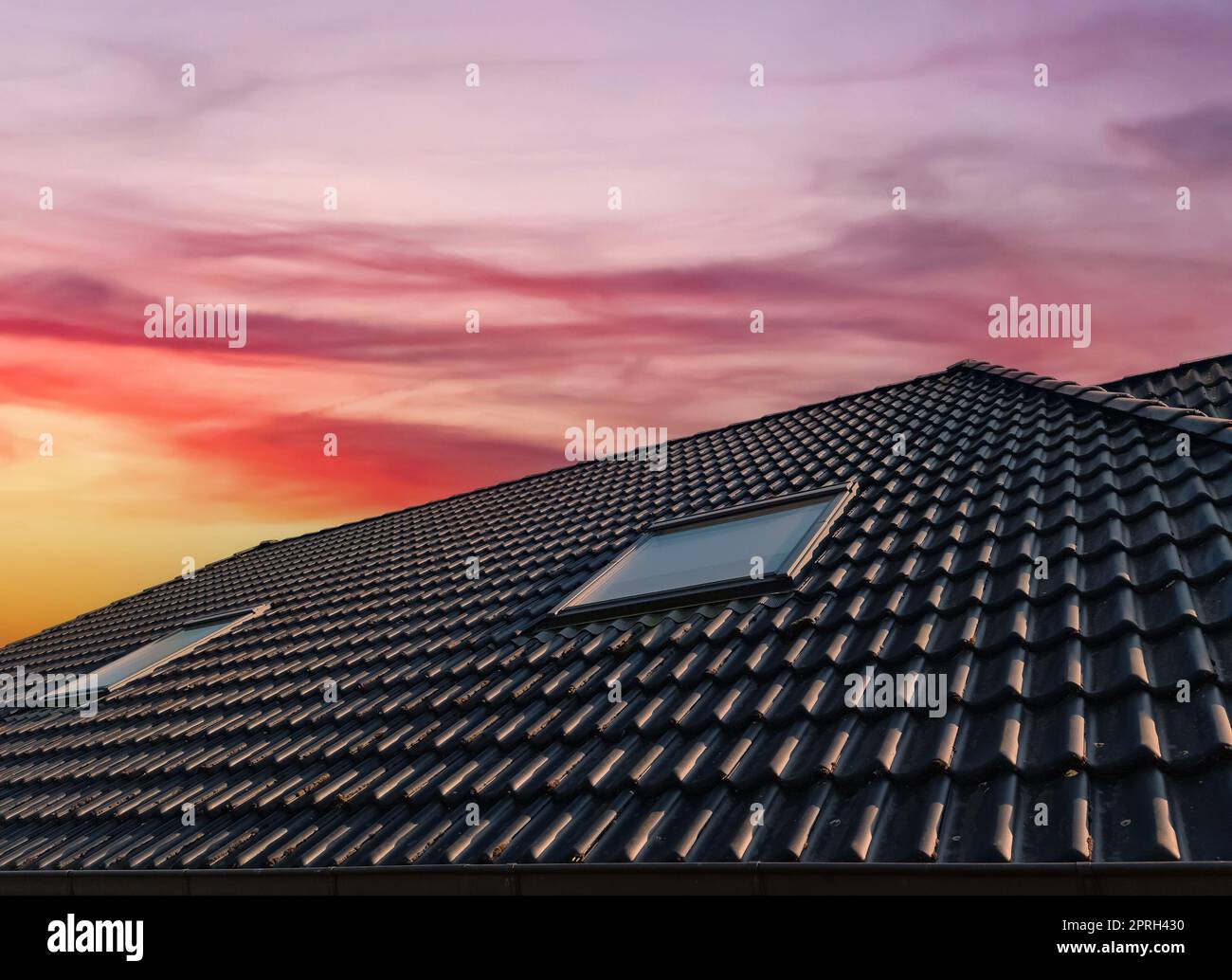 Open roof window in velux style with black roof tiles during sunset