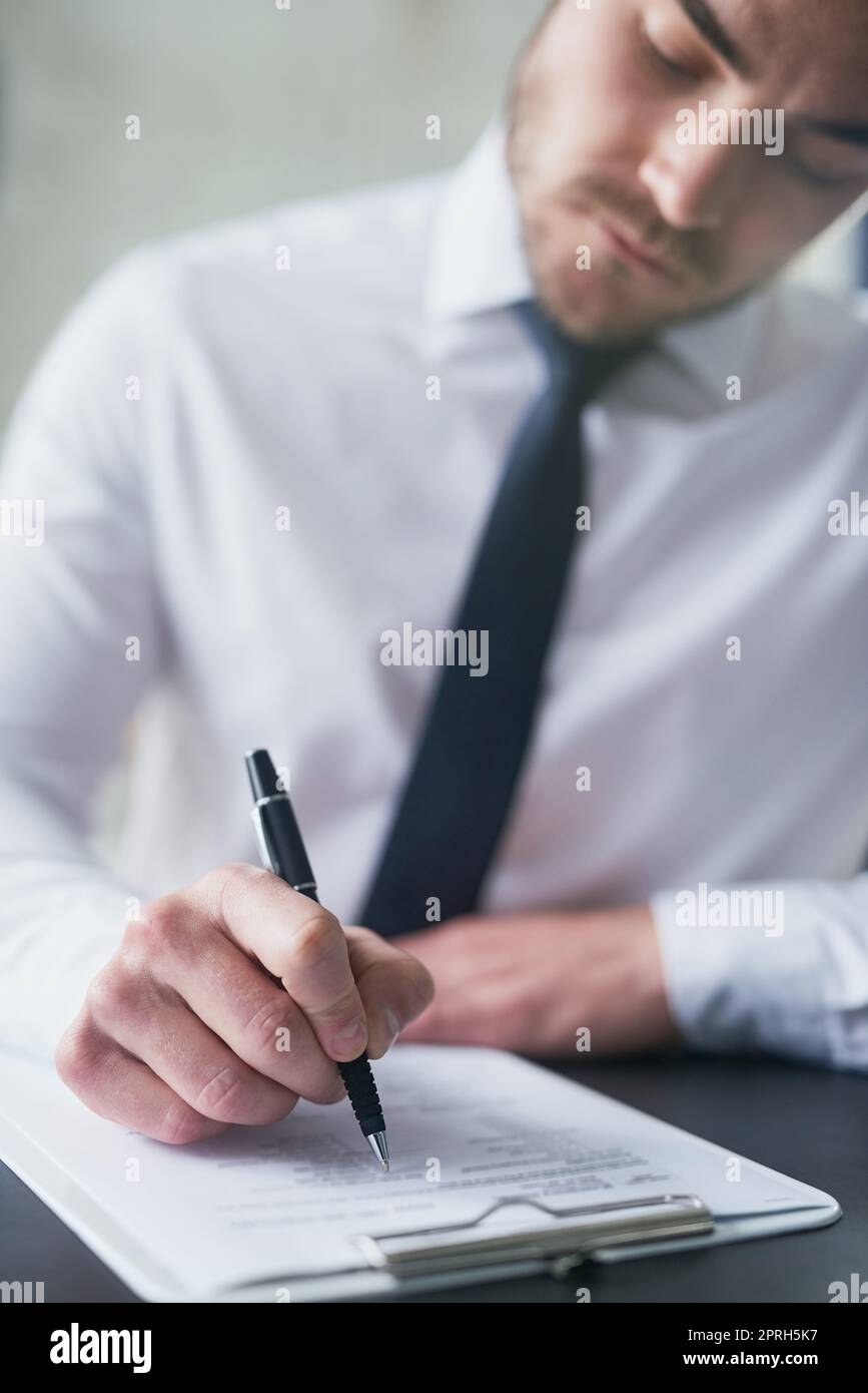 Hes well prepared for this questionnaire. a young businessman filling out paperwork on a clipboard while sitting at a table in an office. Stock Photo