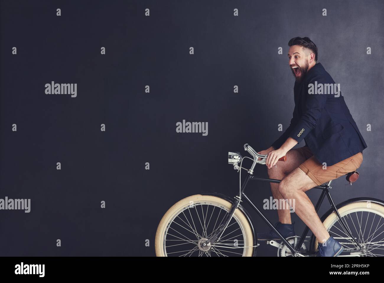 Bicycles fill him with childlike joy. a trendy young man riding a bicycle in studio. Stock Photo