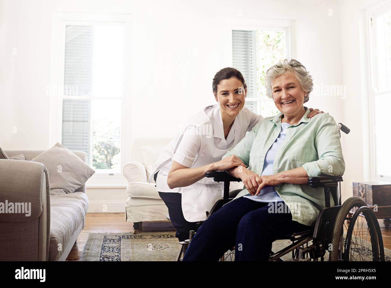 Support with a smile. Portrait of a smiling caregiver and a senior woman in a wheelchair at home. Stock Photo