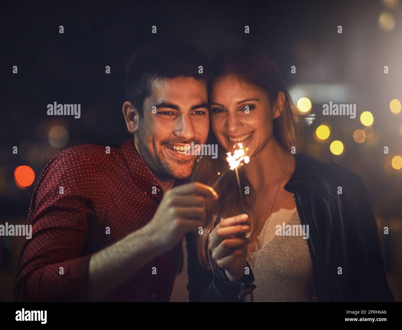 Find a love that makes you sparkle. a happy young couple celebrating with sparklers outside at night. Stock Photo