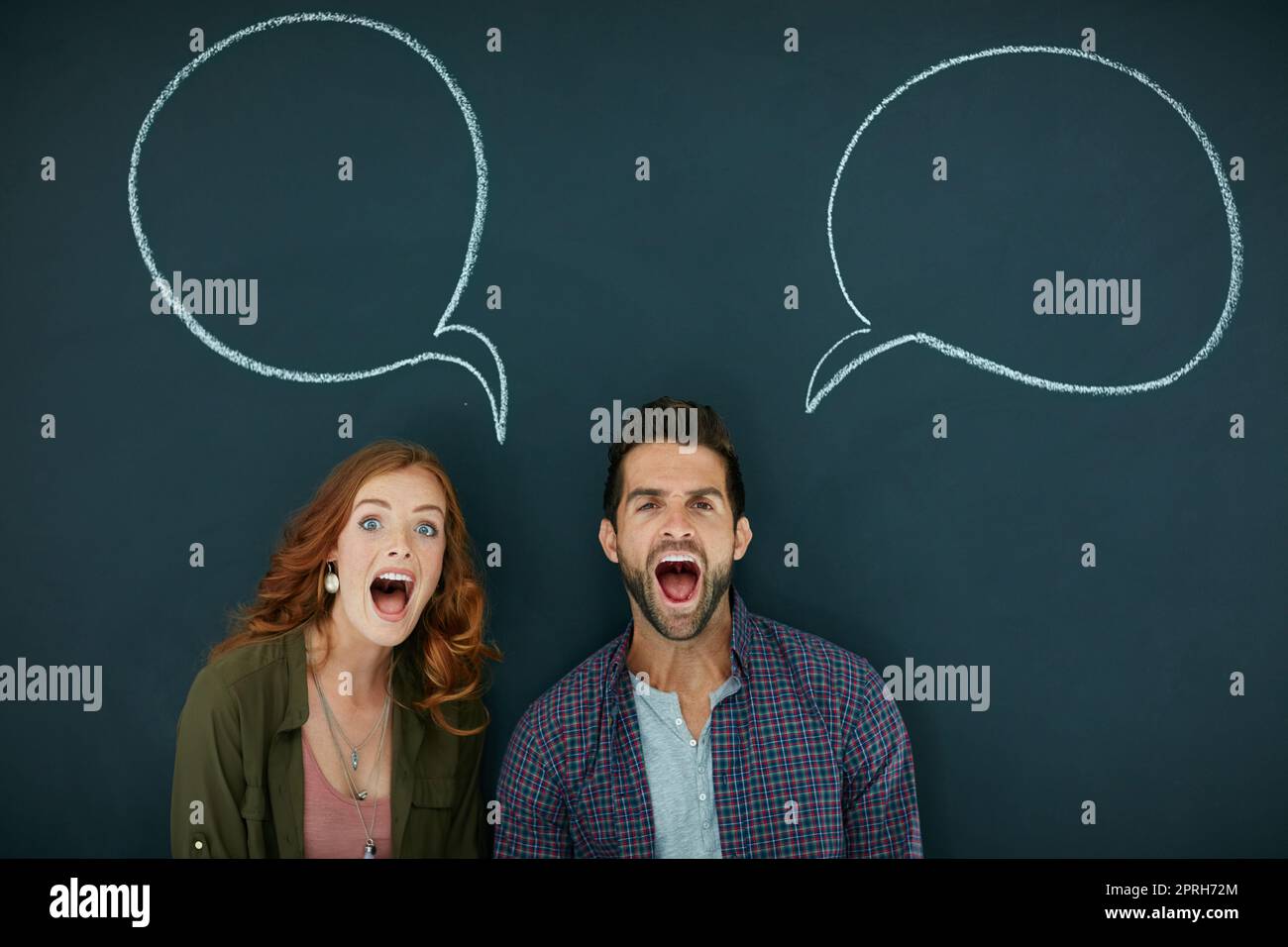 Weve got a lot to shout about. Portrait of a young couple standing in front of a blackboard with speech bubbles drawn on it. Stock Photo