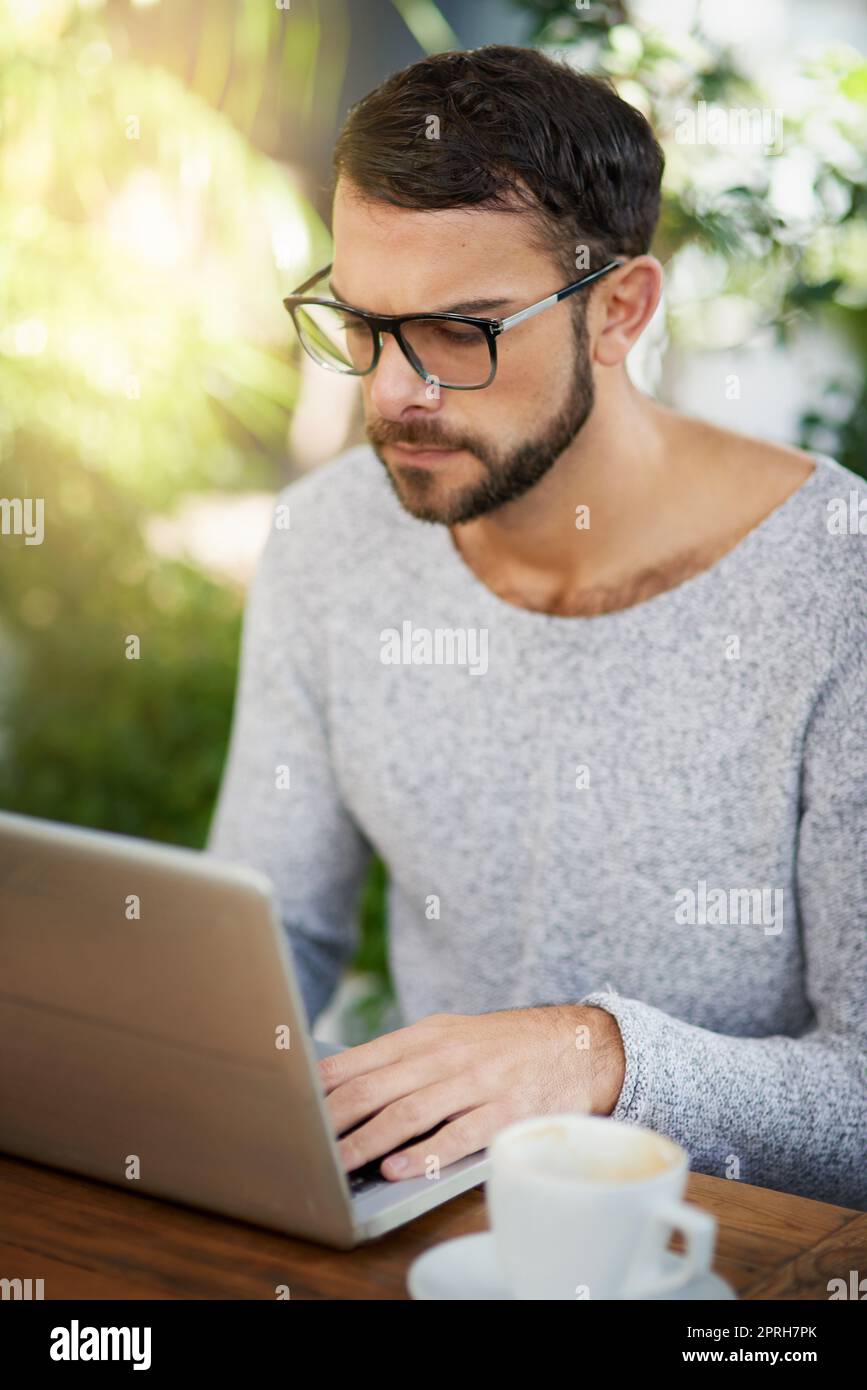In the wifi zone. a handsome young man using a laptop at an outdoor cafe. Stock Photo