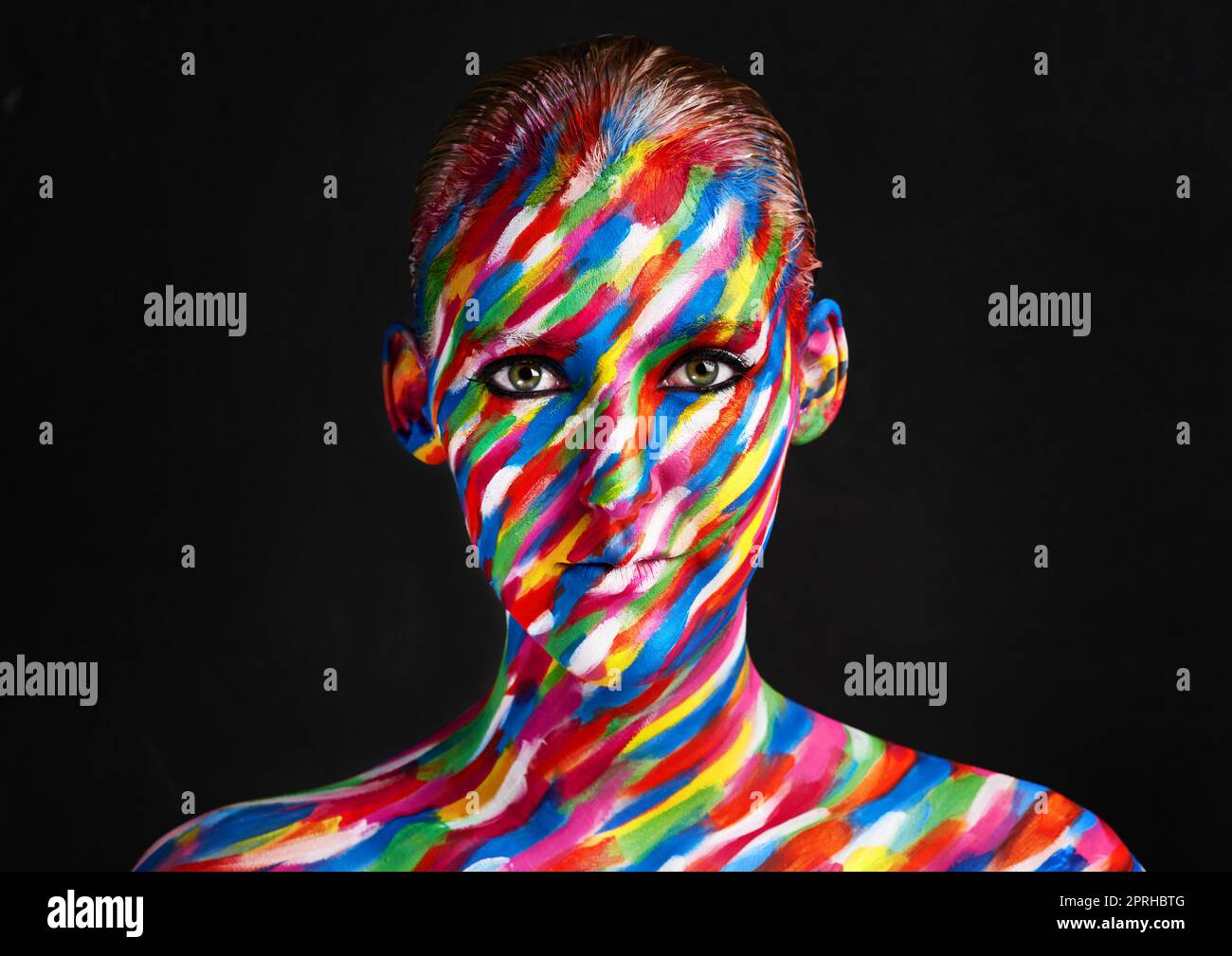 Be your own kind of beautiful. Studio shot of a young woman posing with brightly colored paint on her face against a black background. Stock Photo