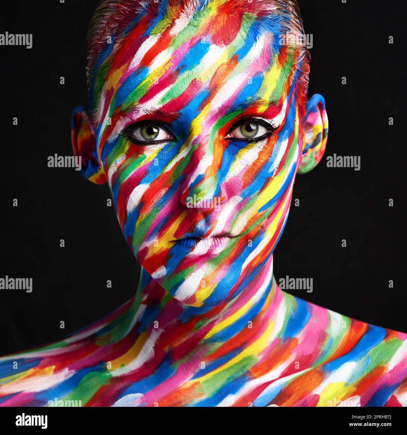 Color that pops. Studio shot of a young woman posing with brightly colored paint on her face against a black background. Stock Photo