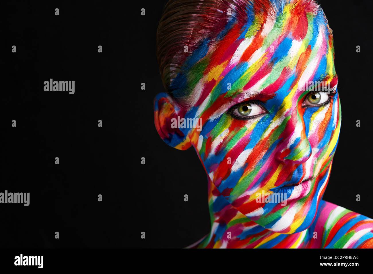 Colors speak louder than words. Studio shot of a young woman posing with brightly colored paint on her face against a black background. Stock Photo
