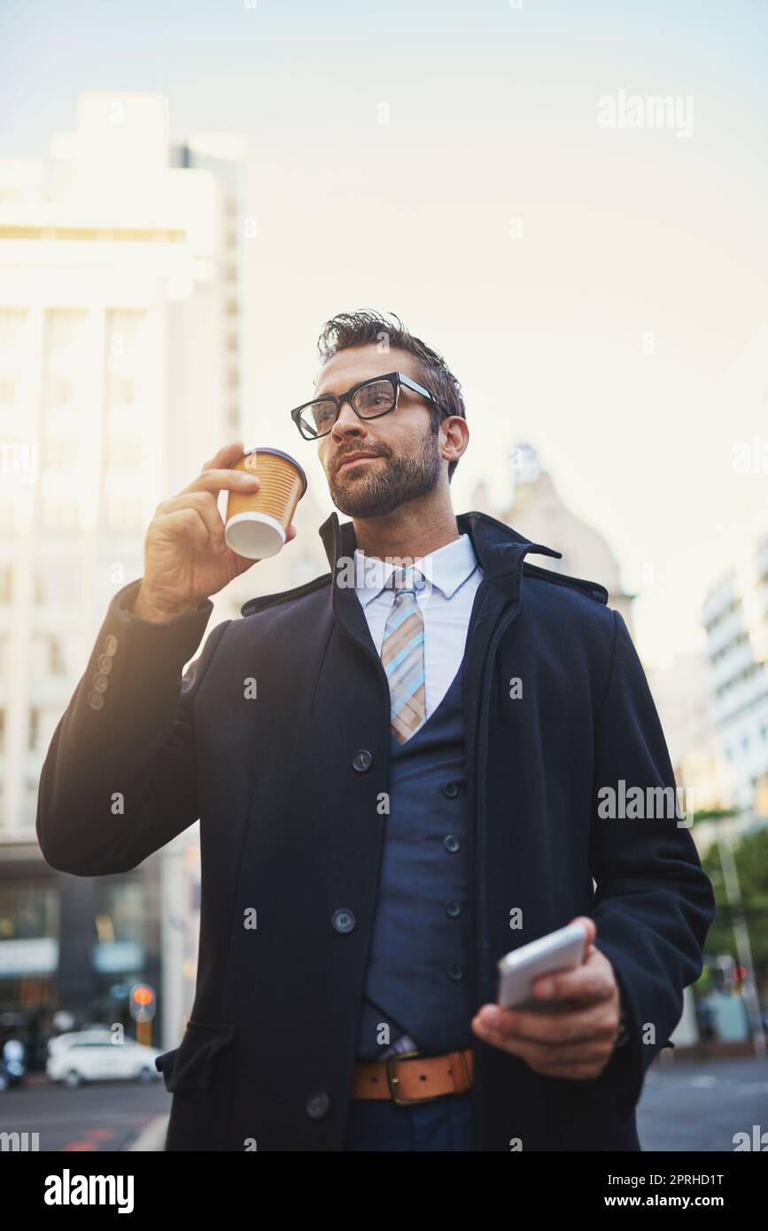 Coffee gives him mojo when hes on the go. a stylish man drinking a cup of coffee while out in the city. Stock Photo