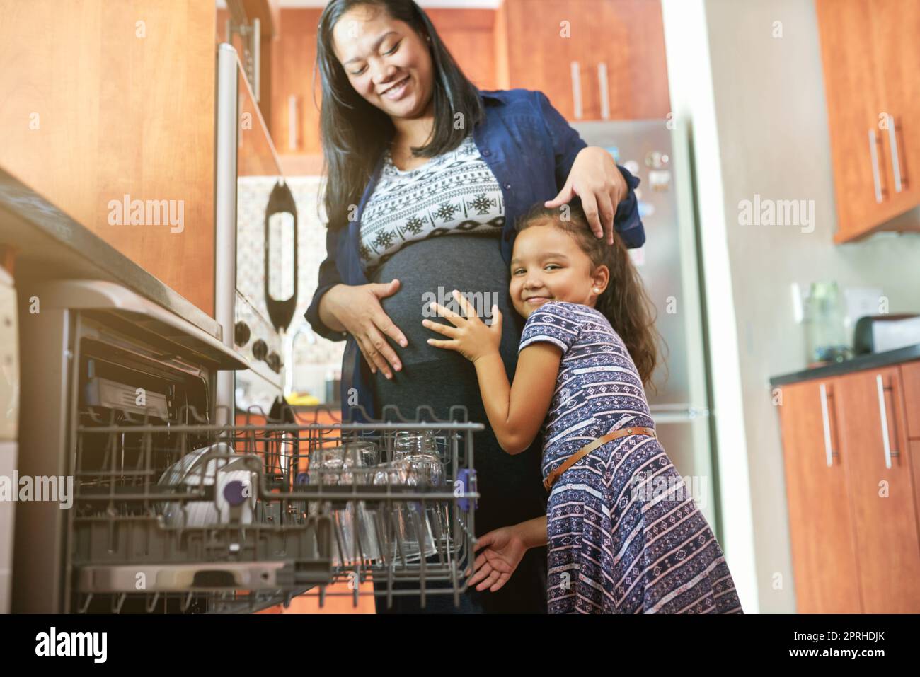 Soon mommy will have another little angel. Portrait of a daughter hugging her pregnant mother in the kitchen. Stock Photo