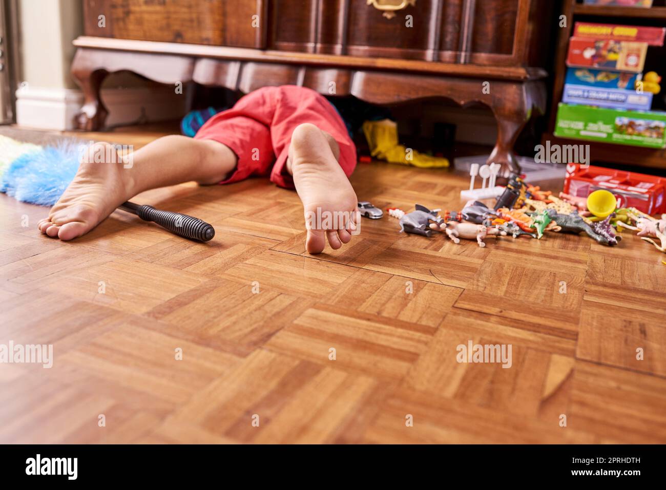 Theres something under here. a young boy on the floor with his feet sticking out from underneath a cupboard. Stock Photo