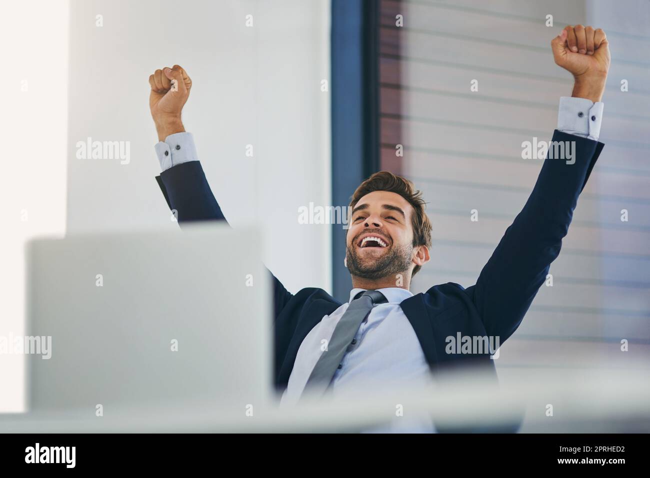 Success has him feeling on top of the world. a young businessman cheering while working in an office. Stock Photo