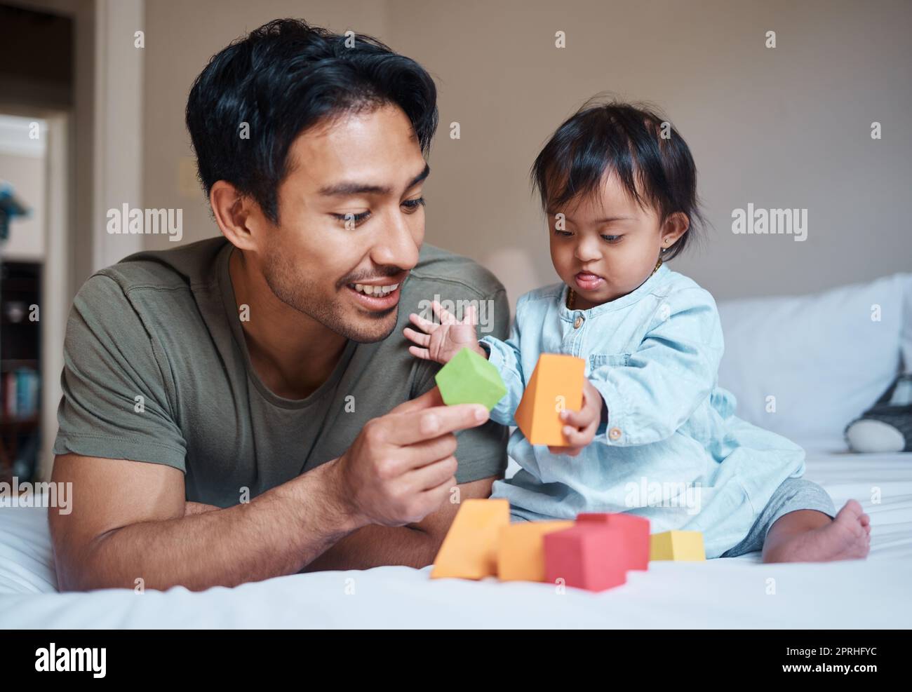 Baby, down syndrome and learning on a bed with child and father playing