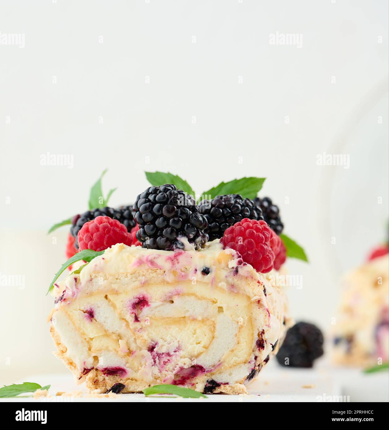 Baked meringue roll with cream and fresh fruits on a white wooden board