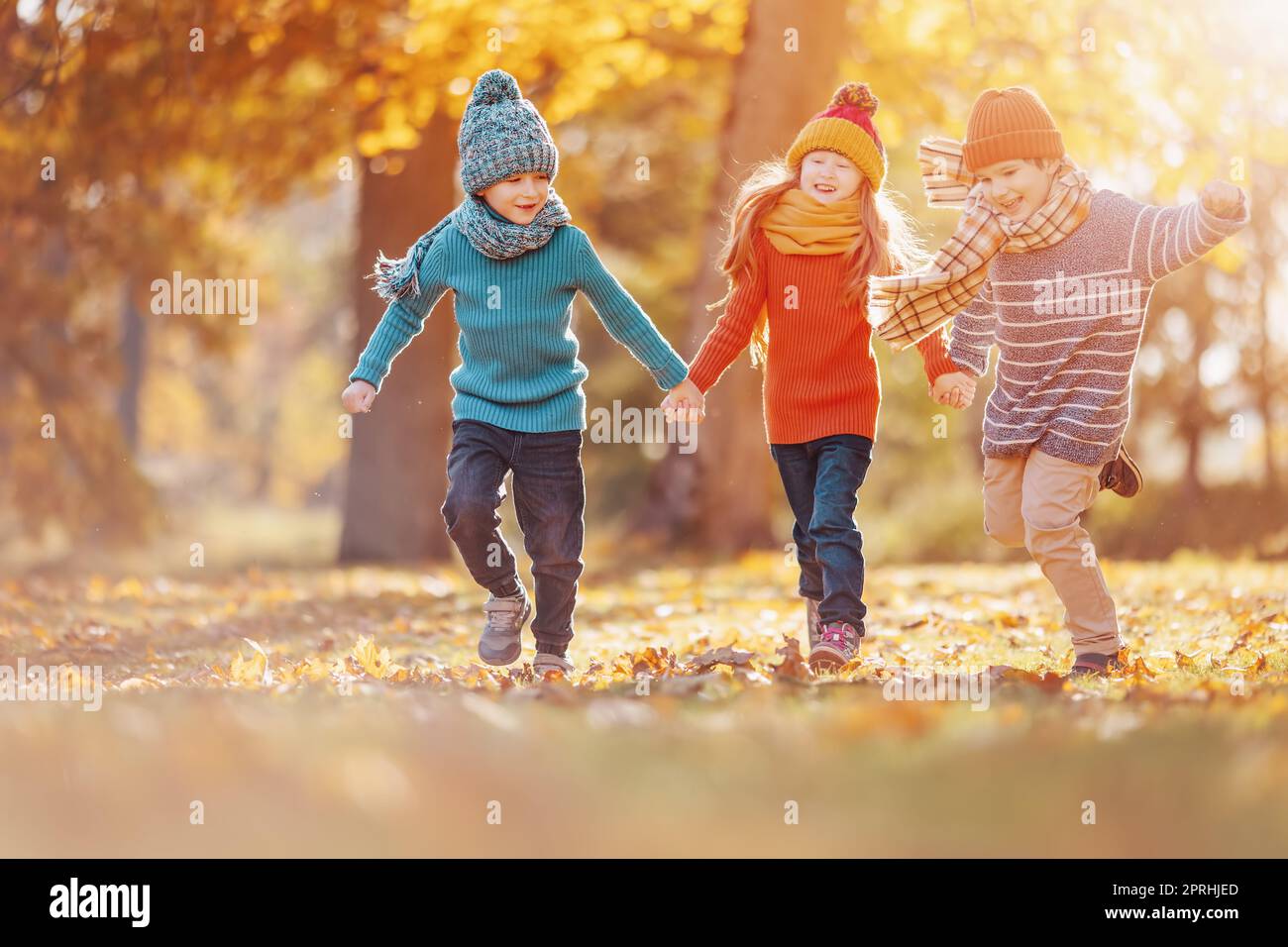 Three children running hand in hand in autumnal park Stock Photo