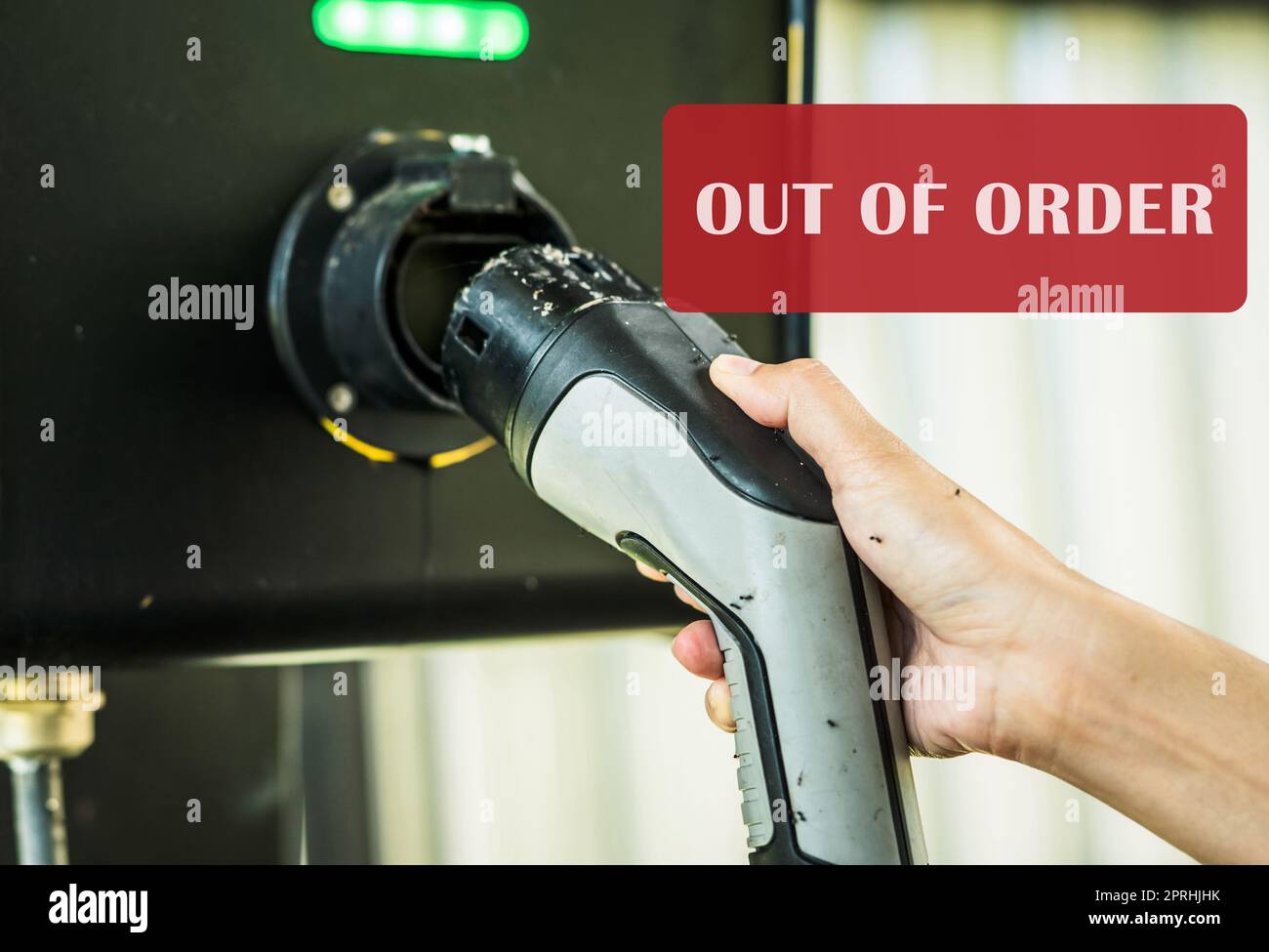 Out of order electric vehicle charging station. Electric vehicle charging station infrastructure problems. Hand holding EV charger that hasn't been used for a long time until the ants come to nest. Stock Photo