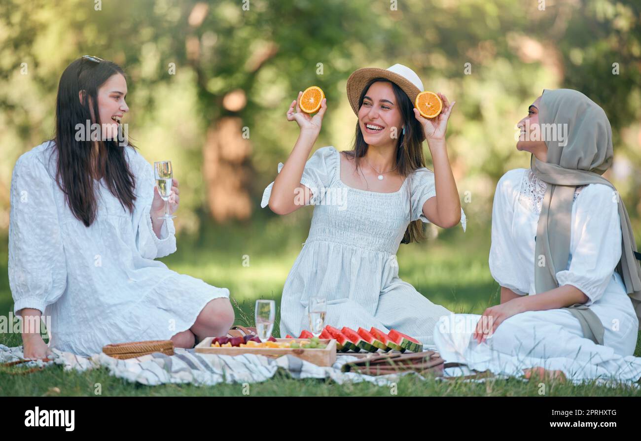Diversity, Islamic and friends on a fruit picnic on grass in nature enjoying orange, watermelon and fun jokes. Muslim, smile and happy women laughing Stock Photo