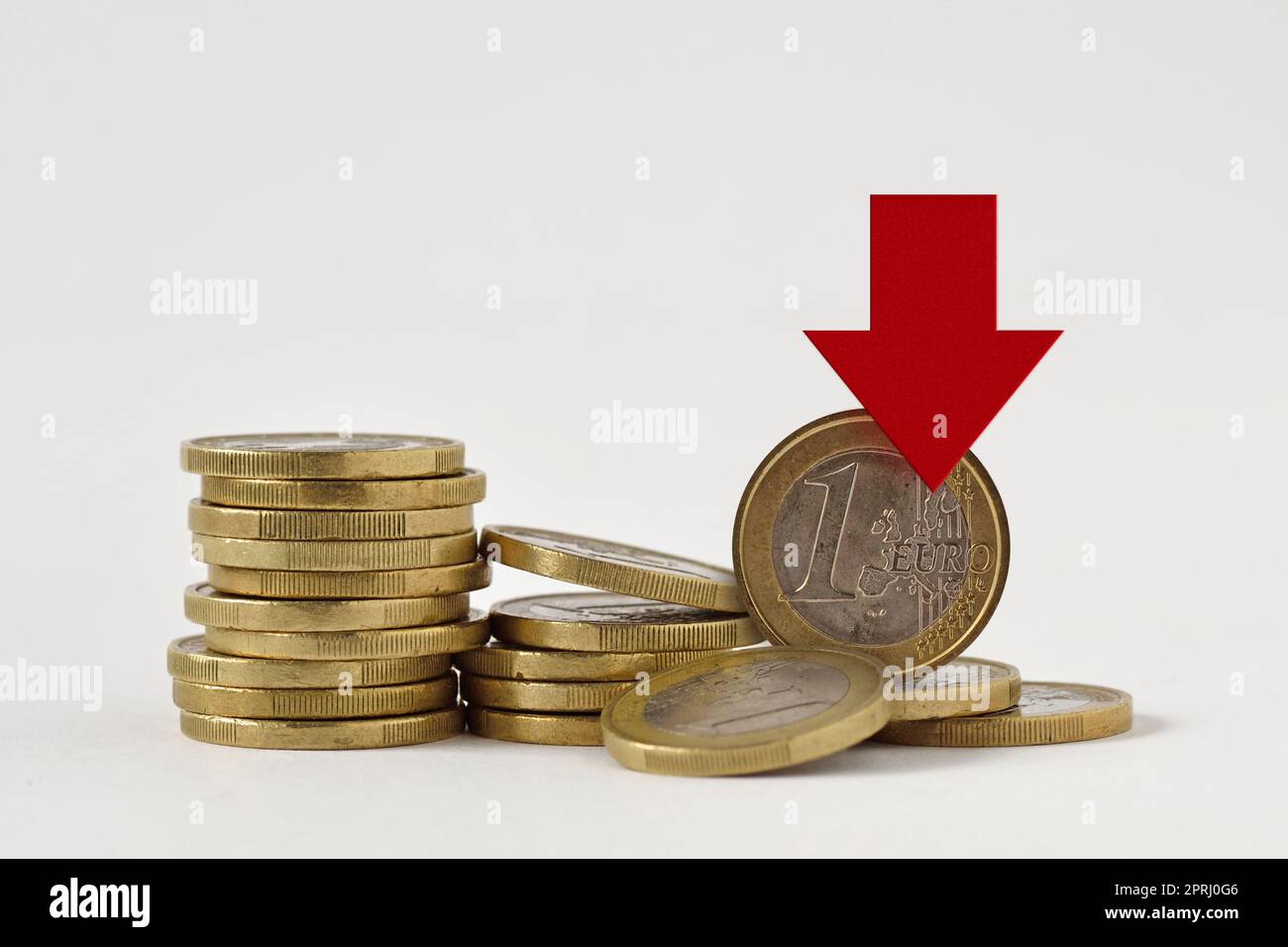 Piles of euro coins with red decreasing arrow on white background - Concept of decrease in euro value and loss of money Stock Photo