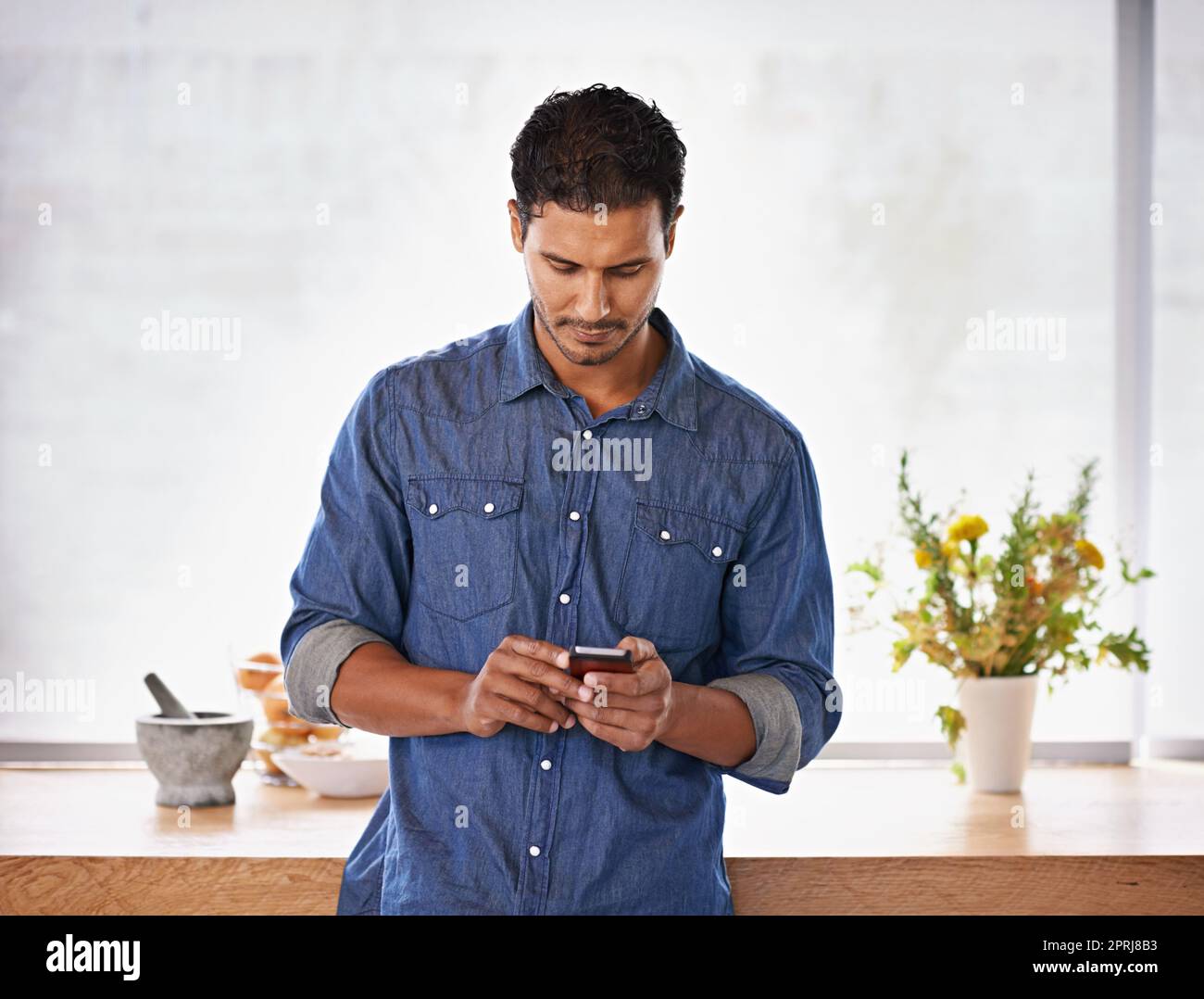 Inviting some guests for dinner. a handsome man typing a text message in the kitchen Stock Photo