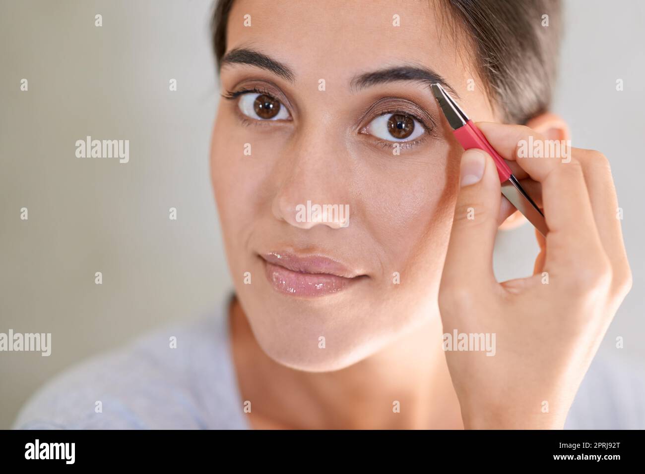 Getting rid of unwanted hairs. A young woman tweezing her eyebrows